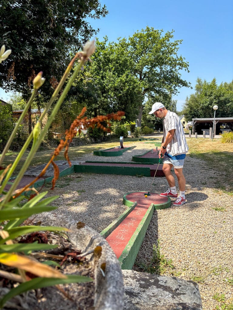 Personne jouant au mini-golf en extérieur, journée ensoleillée.